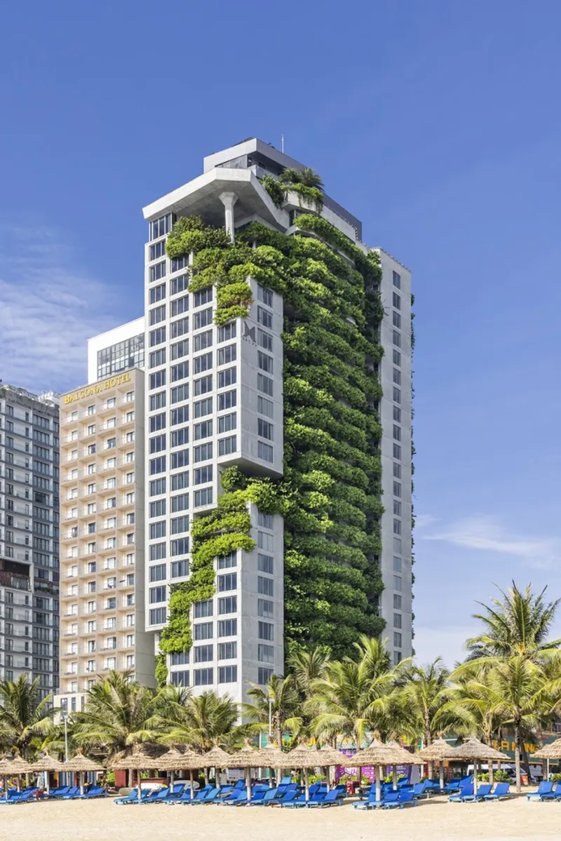 Tower facade with vertical garden strip rising through white balconies above a sandy beach