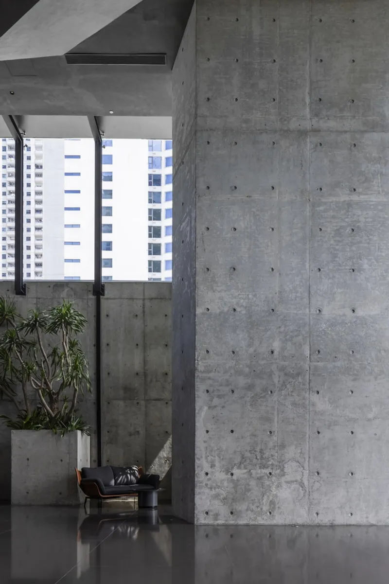 Double-height lobby with board-formed concrete walls and a potted plant beside a chair