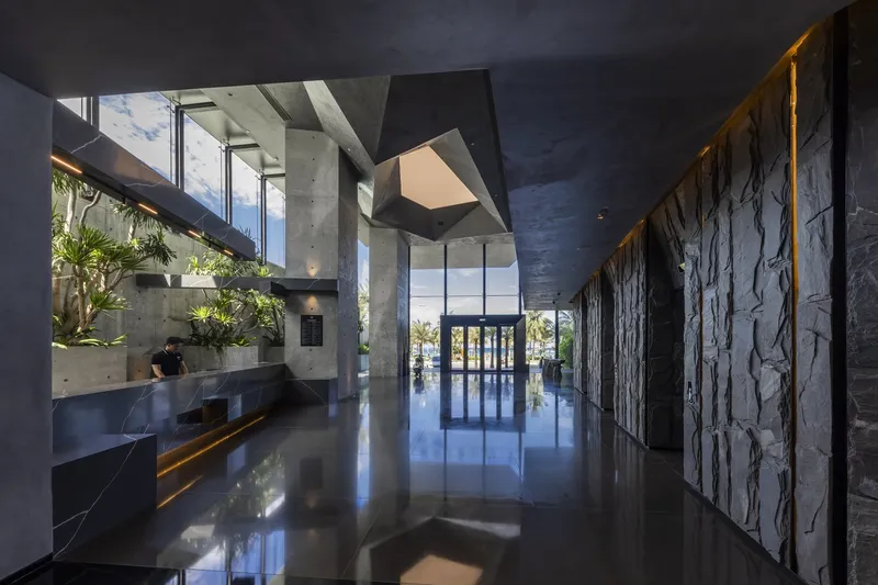 Polished concrete lobby floor reflecting angular ceiling volumes and dark textured stone wall panels
