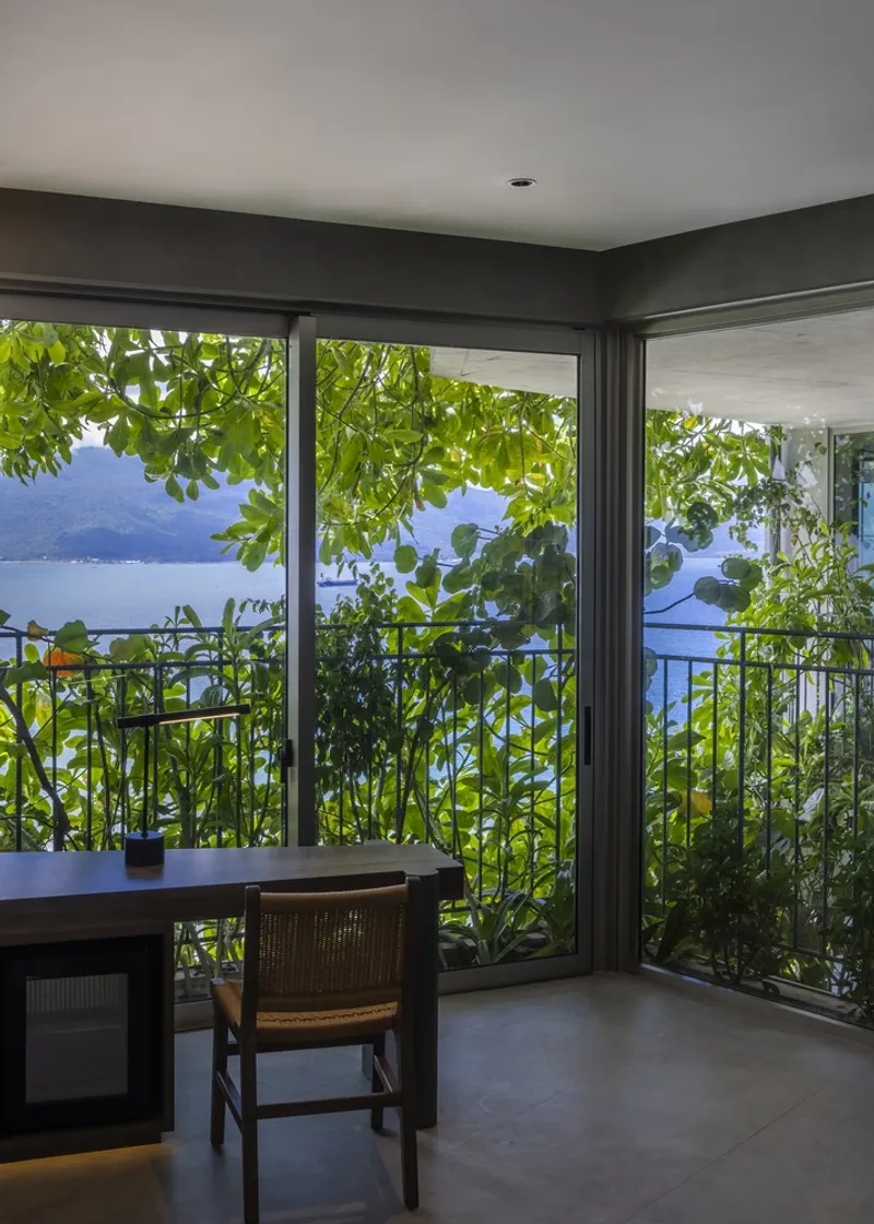 Corner window workspace framed by climbing vines with views across the water to forested hills