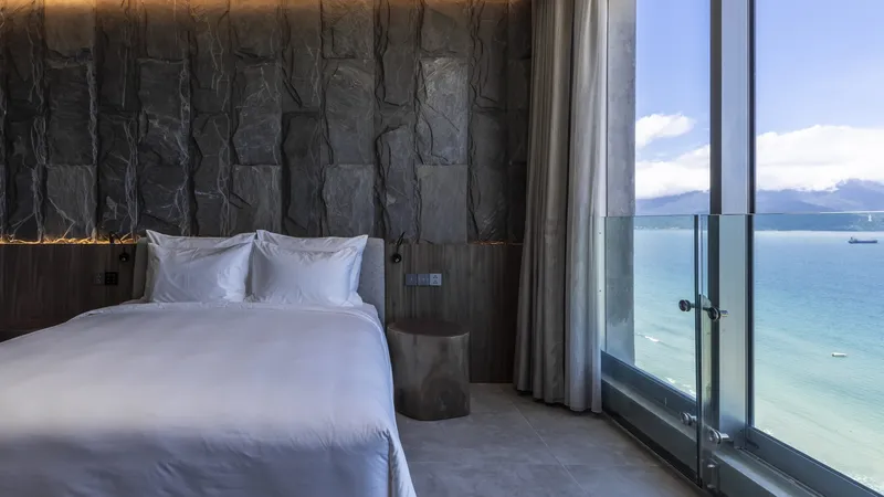 Bedroom view through glass doors to a balcony with ocean and distant mountains visible