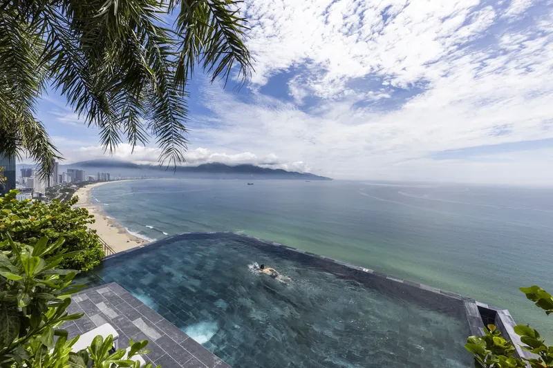 Infinity pool with dark tile framed by palm fronds overlooking a bay and distant mountains