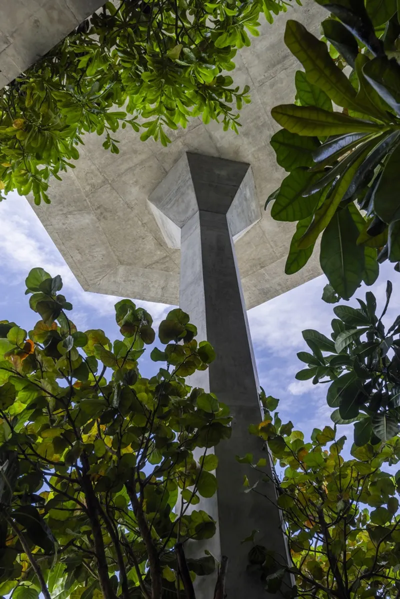 Upward view of concrete underside of balconies with central column surrounded by leafy tropical trees