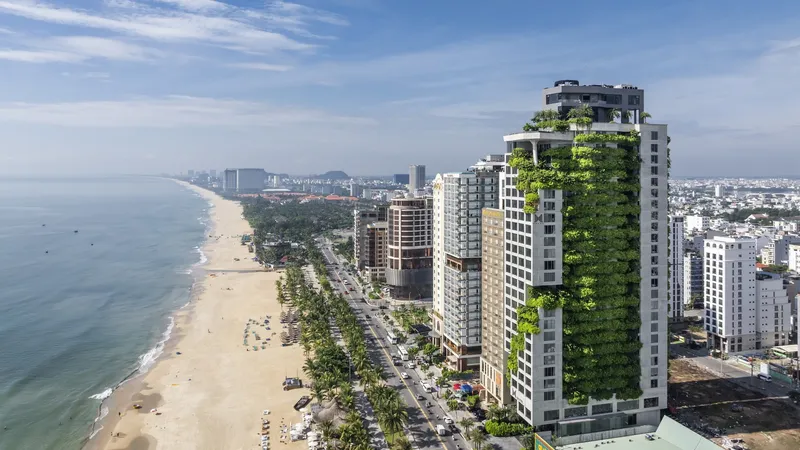 Aerial view of the residential tower with planted facades overlooking the coastline and adjacent buildings