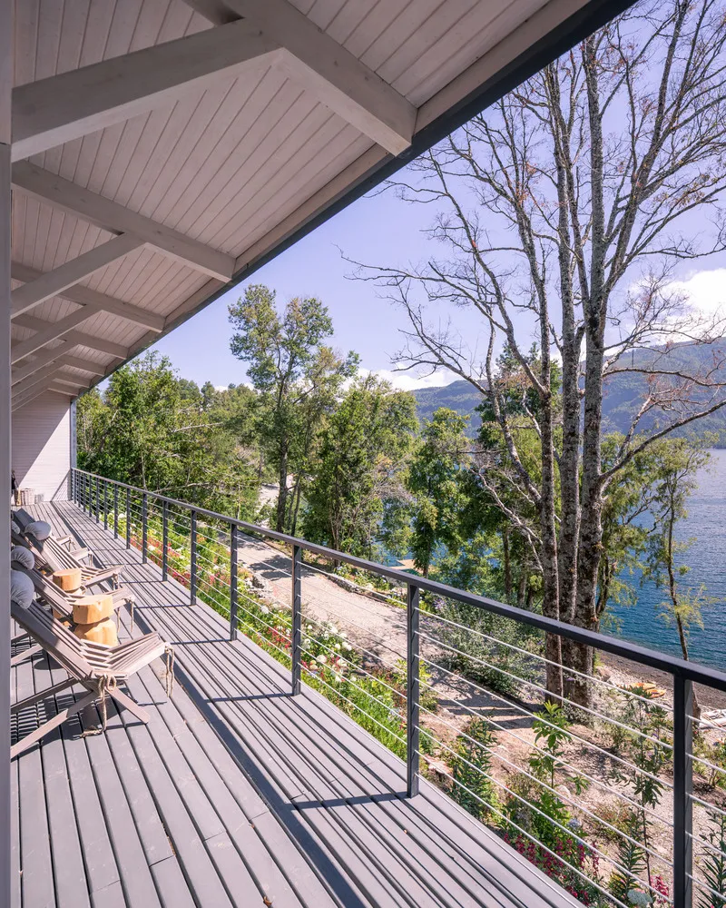 Deck terrace with cable railing overlooking lakefront trees and water under an exposed timber soffit