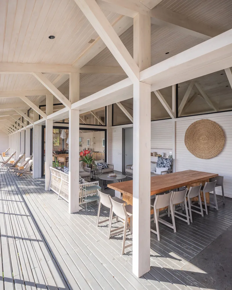 Covered timber deck with white exposed post-and-beam structure and dining area looking toward interior spaces