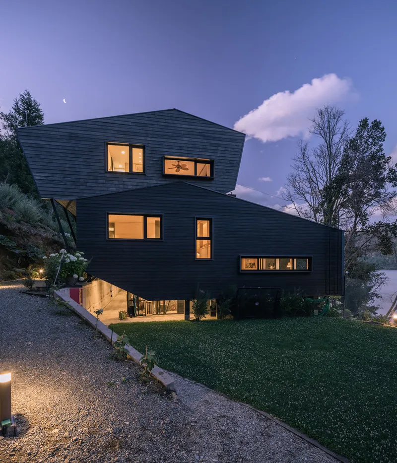 Stacked volumes clad in horizontal black timber siding with glowing interior lights at twilight