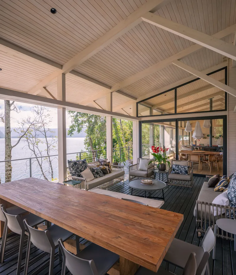 Covered outdoor dining terrace with exposed timber beams and views of the lake through trees