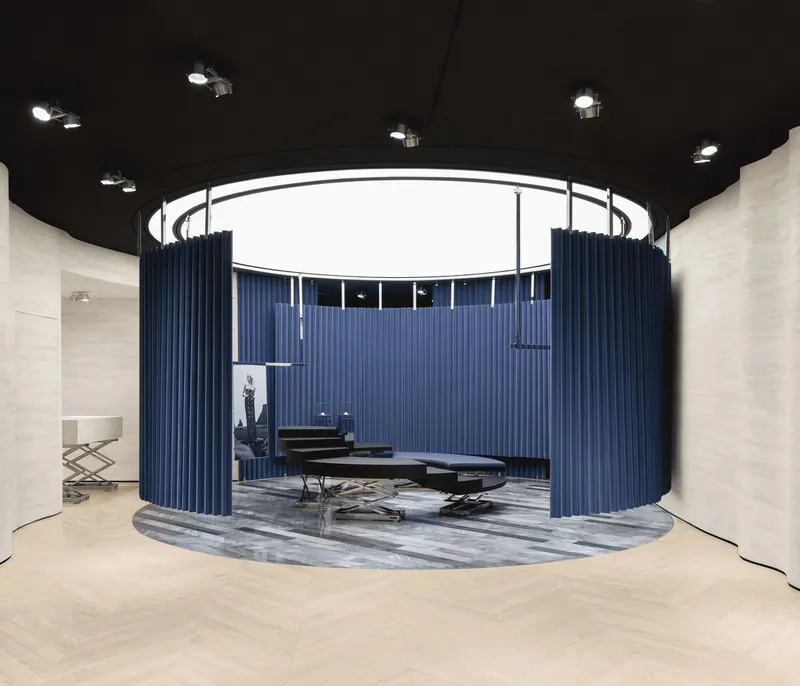 Circular retail display platform with blue fluted curtain walls beneath a black ceiling with circular skylight