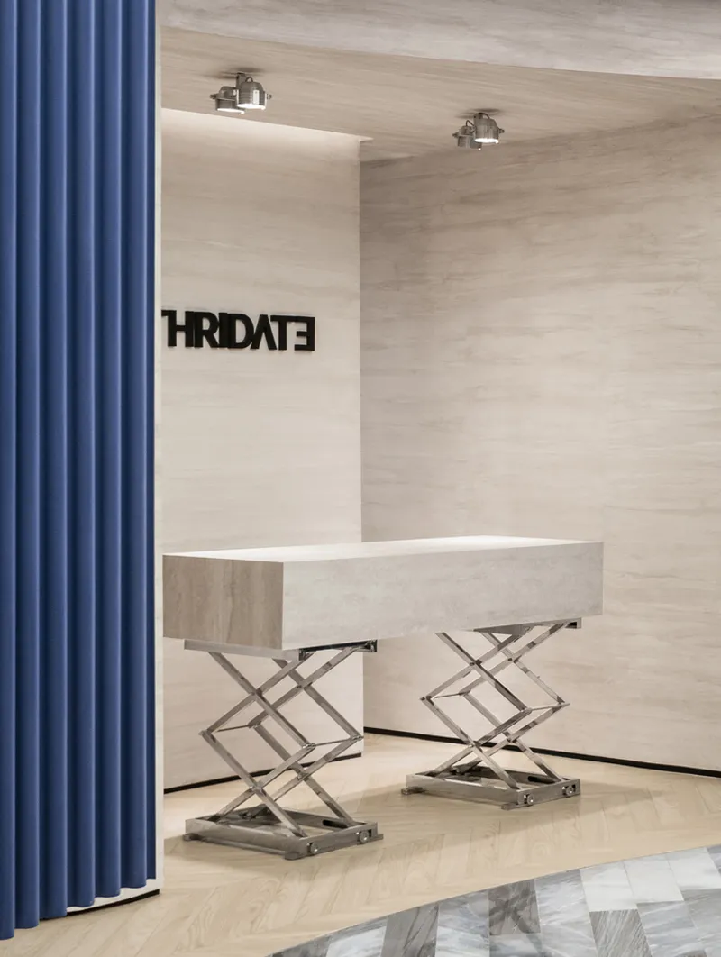 Reception desk on scissor-lift bases against travertine wall with blue curtain at left