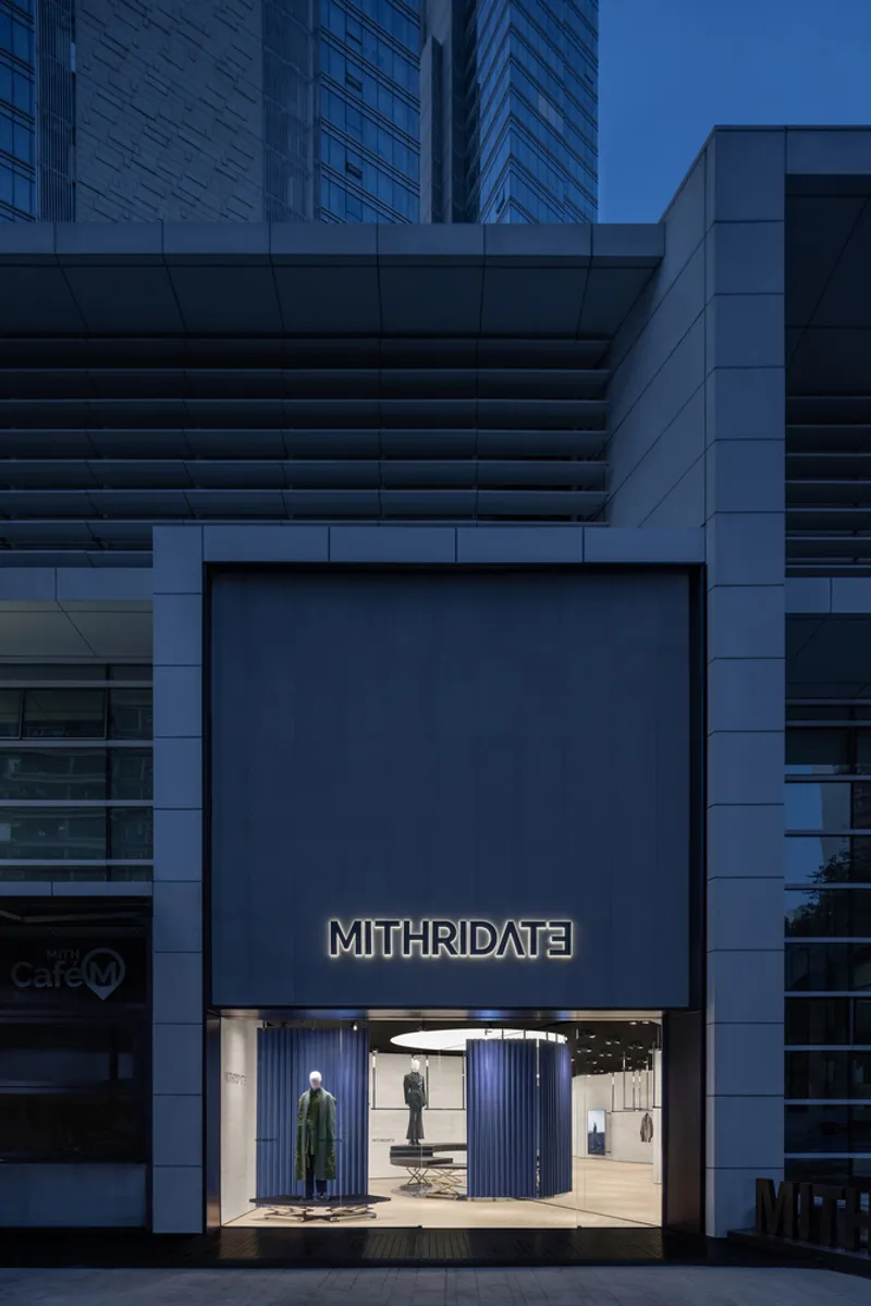 Street-level storefront set within stepped grey panel facade beneath high-rise towers at twilight