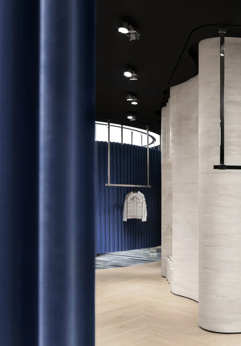 View through vertical blue curtain toward curved corridor with pale wood walls and black track lighting
