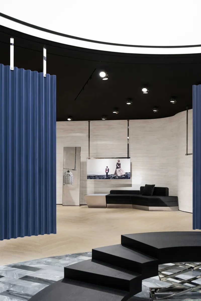 Interior showing black geometric steps, blue curtain dividers and pale wood walls under curved black ceiling