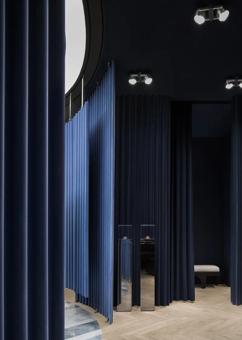 Fitting room corridor with blue and black fabric curtains and curved ceiling mirror above