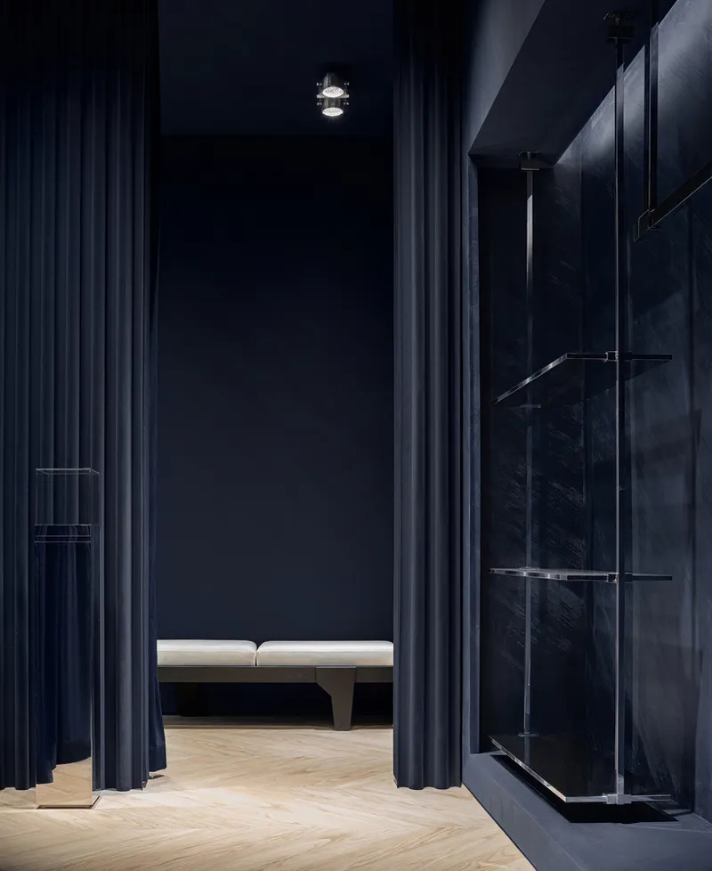 Retail interior hallway with floor-to-ceiling blue curtains and glass display shelving along marble wall