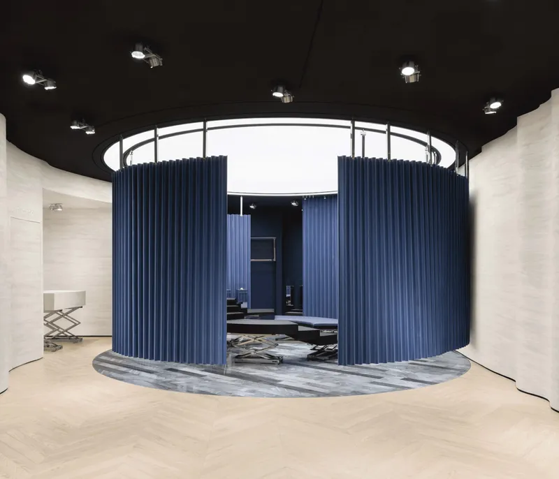 Circular fitting area enclosed by blue pleated curtains beneath a white ring skylight