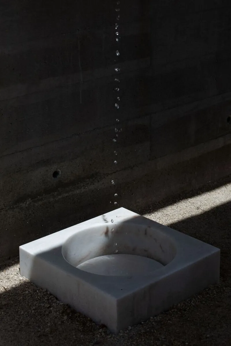 White marble basin catching falling water droplets in a shaft of sunlight