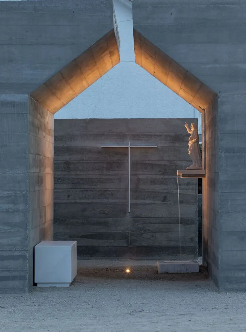 Gable-shaped concrete threshold with white cube basin and glass partition at dusk