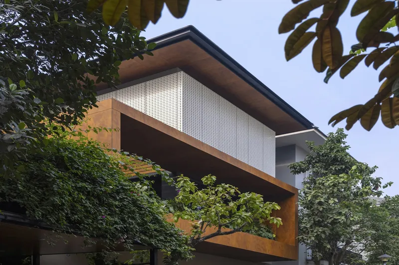 Street view of cantilevered weathered steel volume with perforated metal screen framed by trees