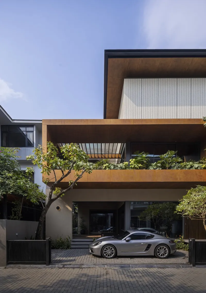 Entry court with parked car beneath cantilevered weathered steel balcony planted with trees