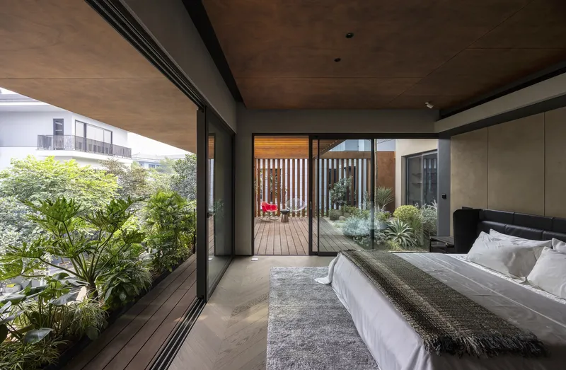 Bedroom opening onto planted terrace through sliding glass doors with timber soffit above