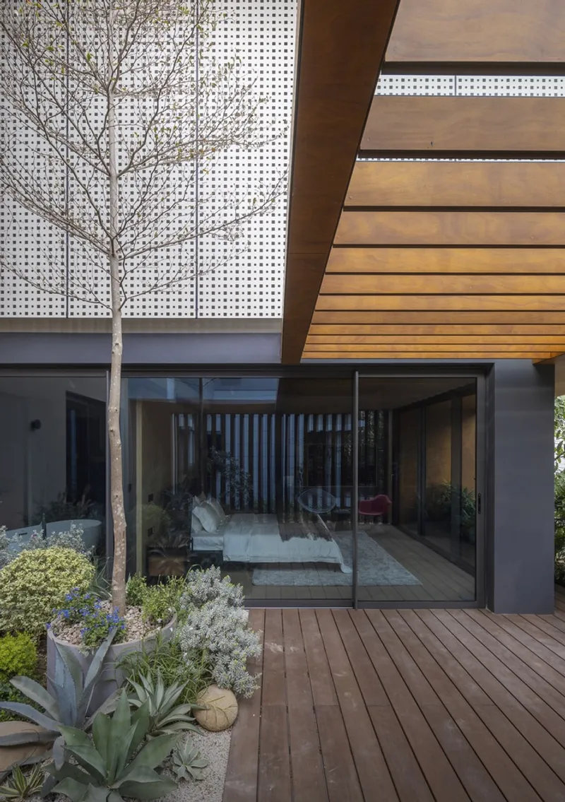 Timber deck terrace with perforated metal screen wall, planted beds and glass sliding doors