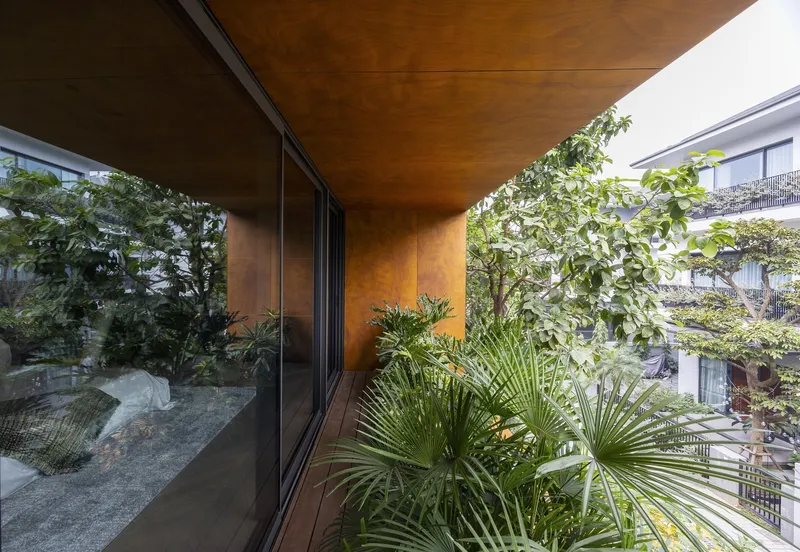 Cantilevered terrace with weathered steel soffit framing a planted balcony with palm fronds