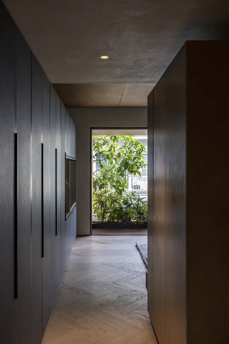 Dark timber corridor with herringbone floor leading to a planted terrace framed by glass doors