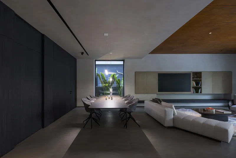 Open-plan living area with dining table, concrete floors and timber ceiling wedge at dusk