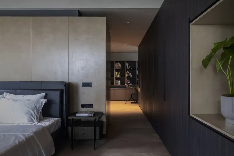 Bedroom with dark timber millwork and glimpse into illuminated study beyond at night