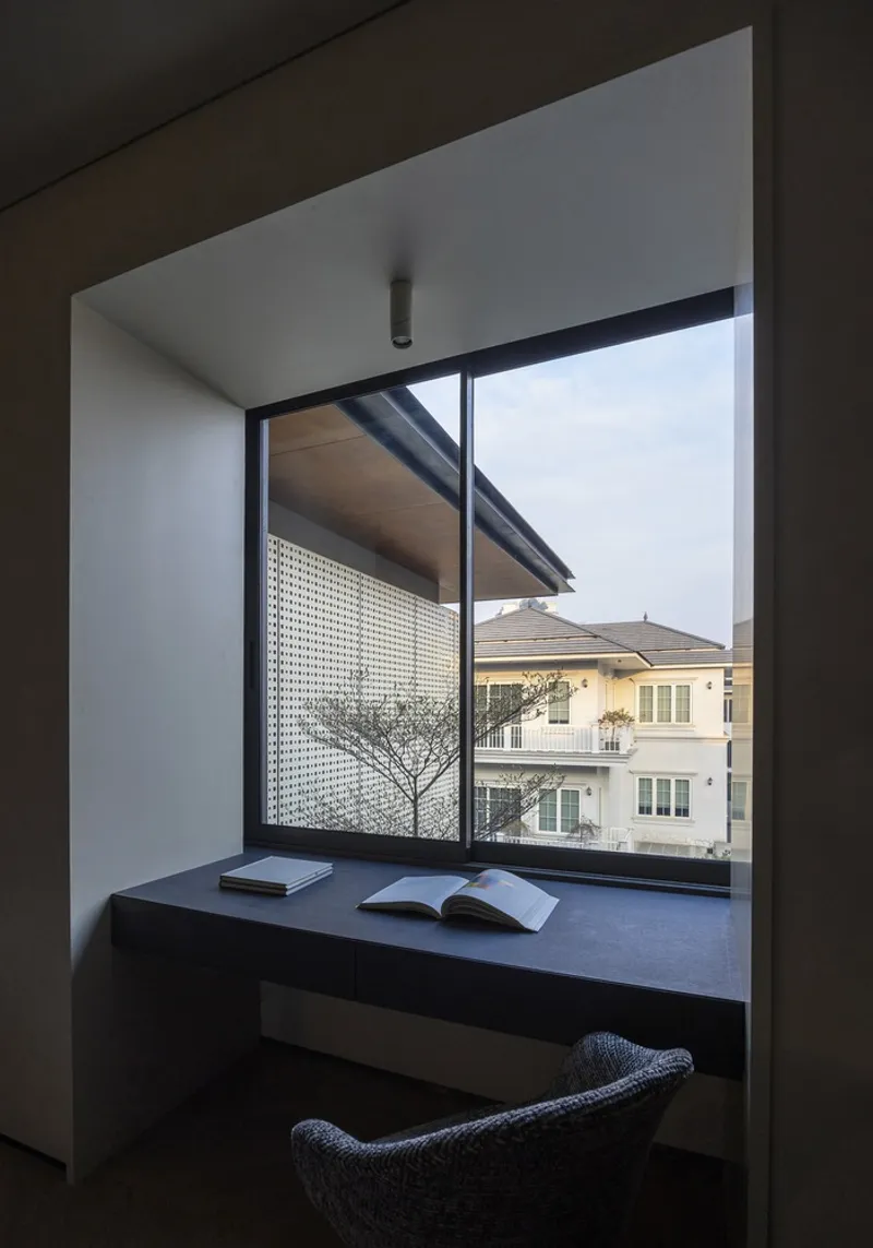Window seat nook with perforated screen overhang and view to neighboring houses under overcast sky