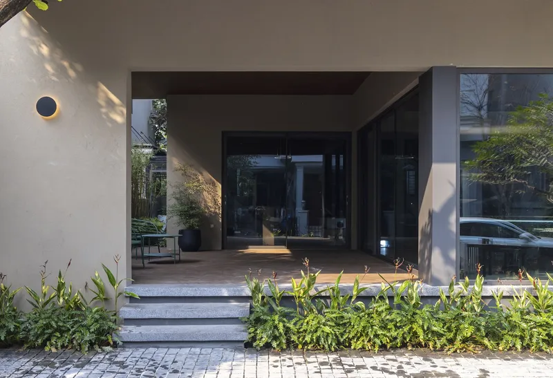 Entrance with concrete steps leading to a recessed threshold flanked by planted beds and dappled sunlight