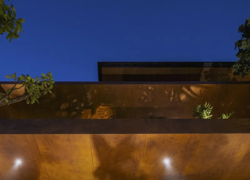 Copper-clad facade with recessed uplighting and planted strip at dusk beneath a deep blue sky
