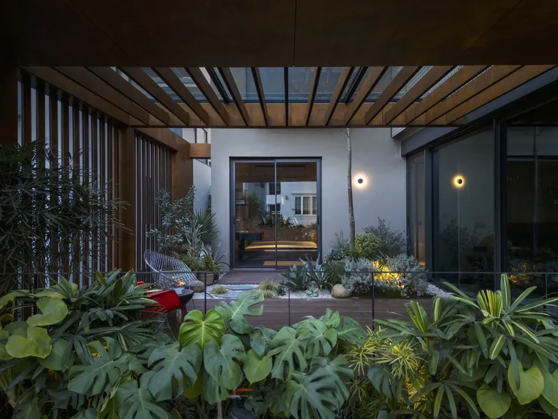 Internal courtyard garden with tropical plantings viewed through slatted timber pergola beams at dusk