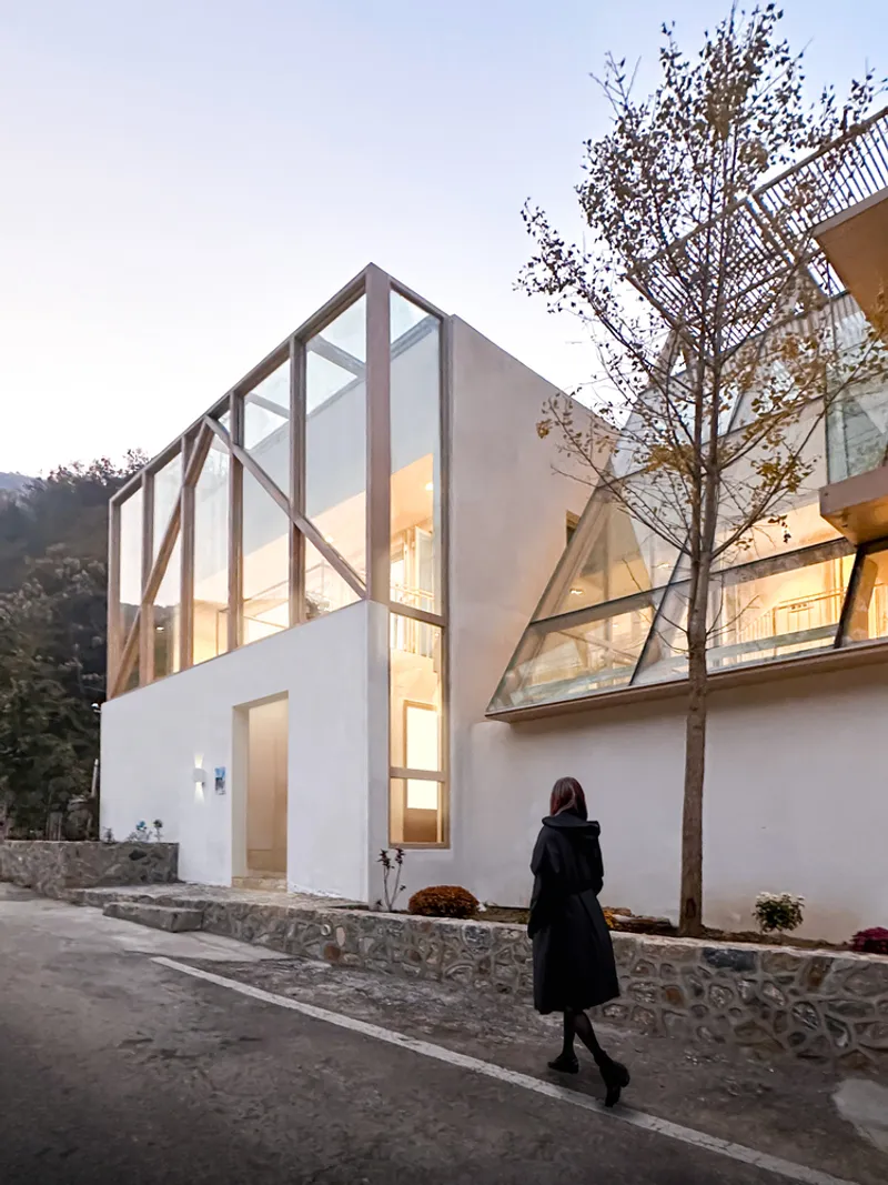 Street view of the glazed gable facade with timber frame behind a stone wall at dusk