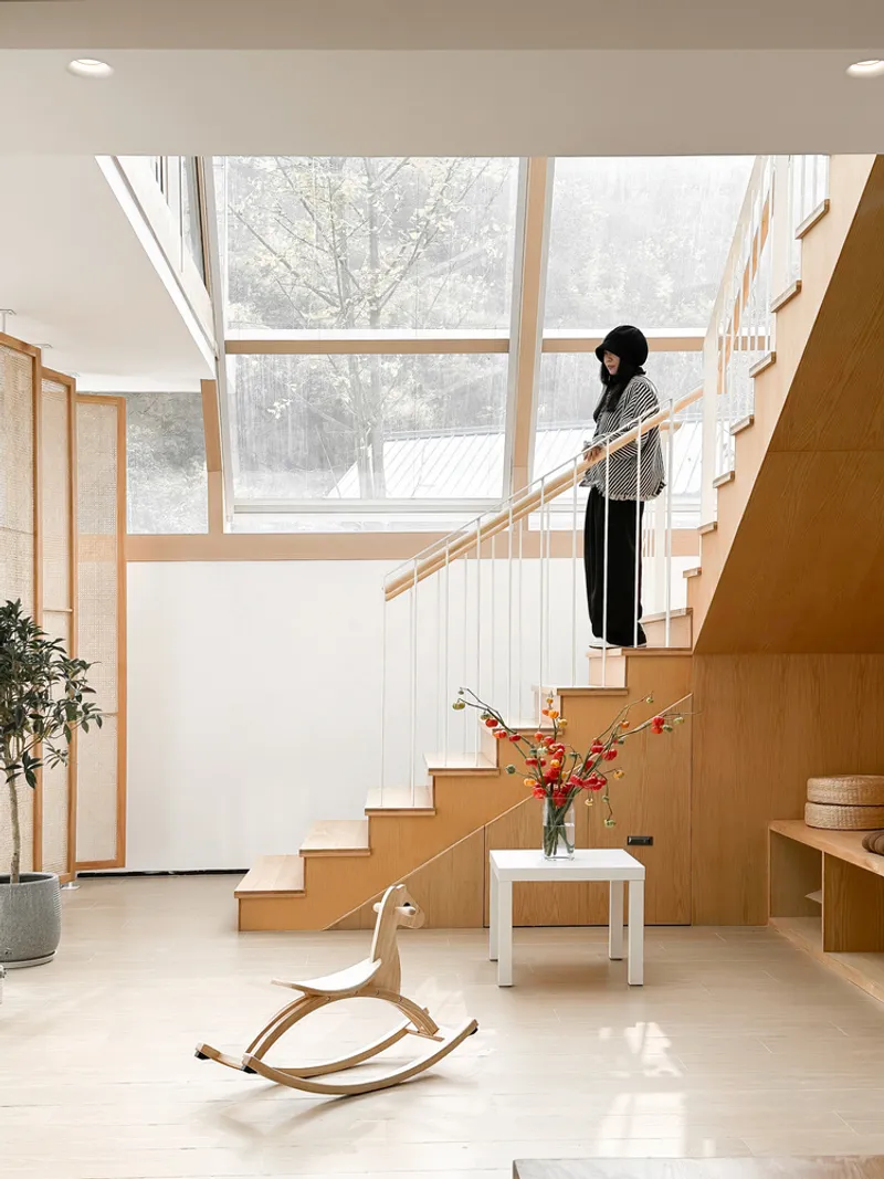 Interior staircase in light timber with a figure descending and winter landscape visible through tall windows