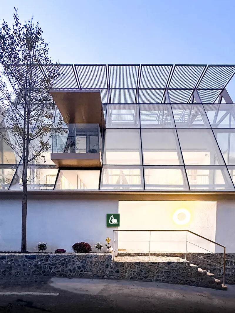 Entrance facade showing the diagonal glazing grid and slatted overhang at twilight beside bare trees