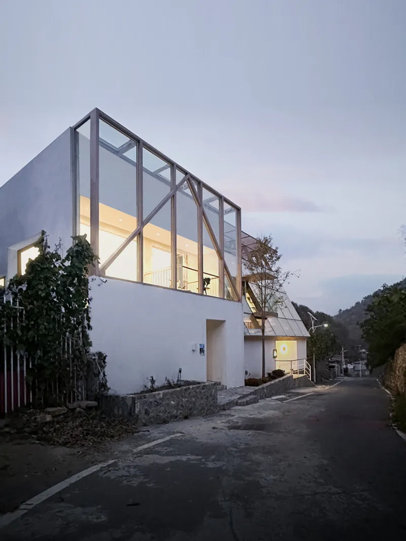 Glazed timber frame facade illuminated from within at dusk on a quiet residential street