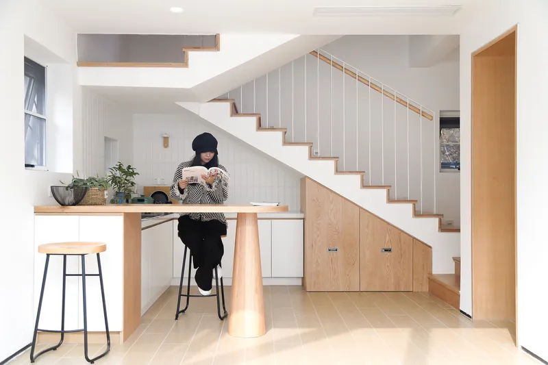 Kitchen counter with conical timber leg beneath the underside of a white-paneled staircase