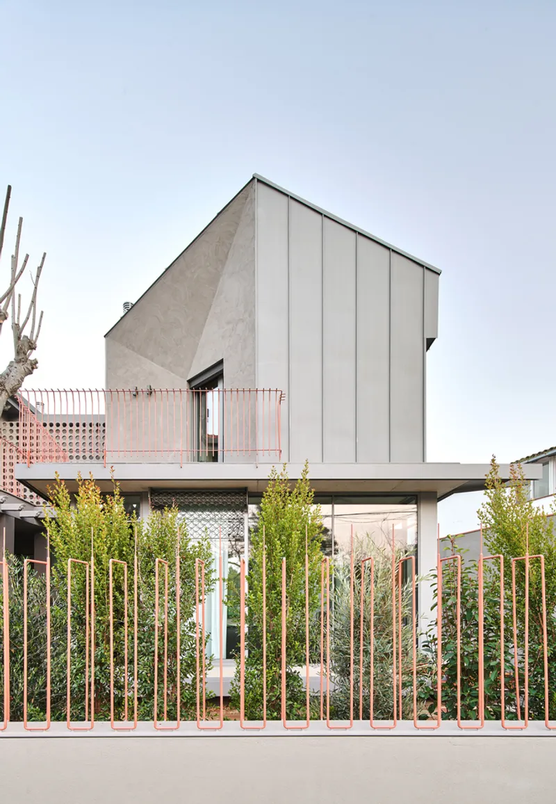 Street facade with metal panel upper volume and perforated copper screen balcony above young plantings