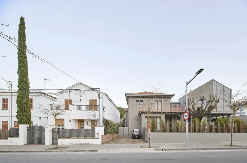Streetscape showing the metal-clad structure among traditional houses with overhead power lines and bare trees