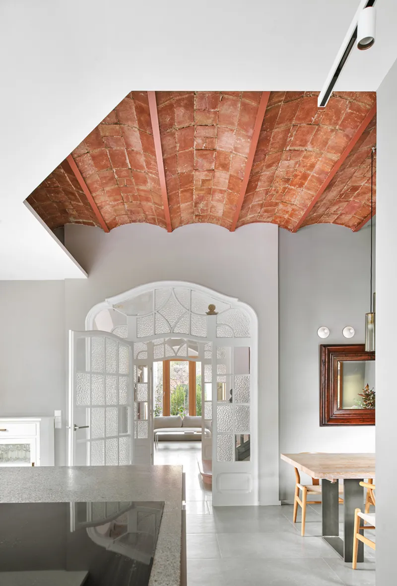Exposed terracotta brick vault ceiling above white archway with textured glass panels in dining area