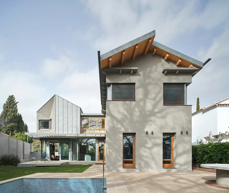 Garden view of the tower volume with timber-lined eaves and horizontal louvers under a cloudy sky