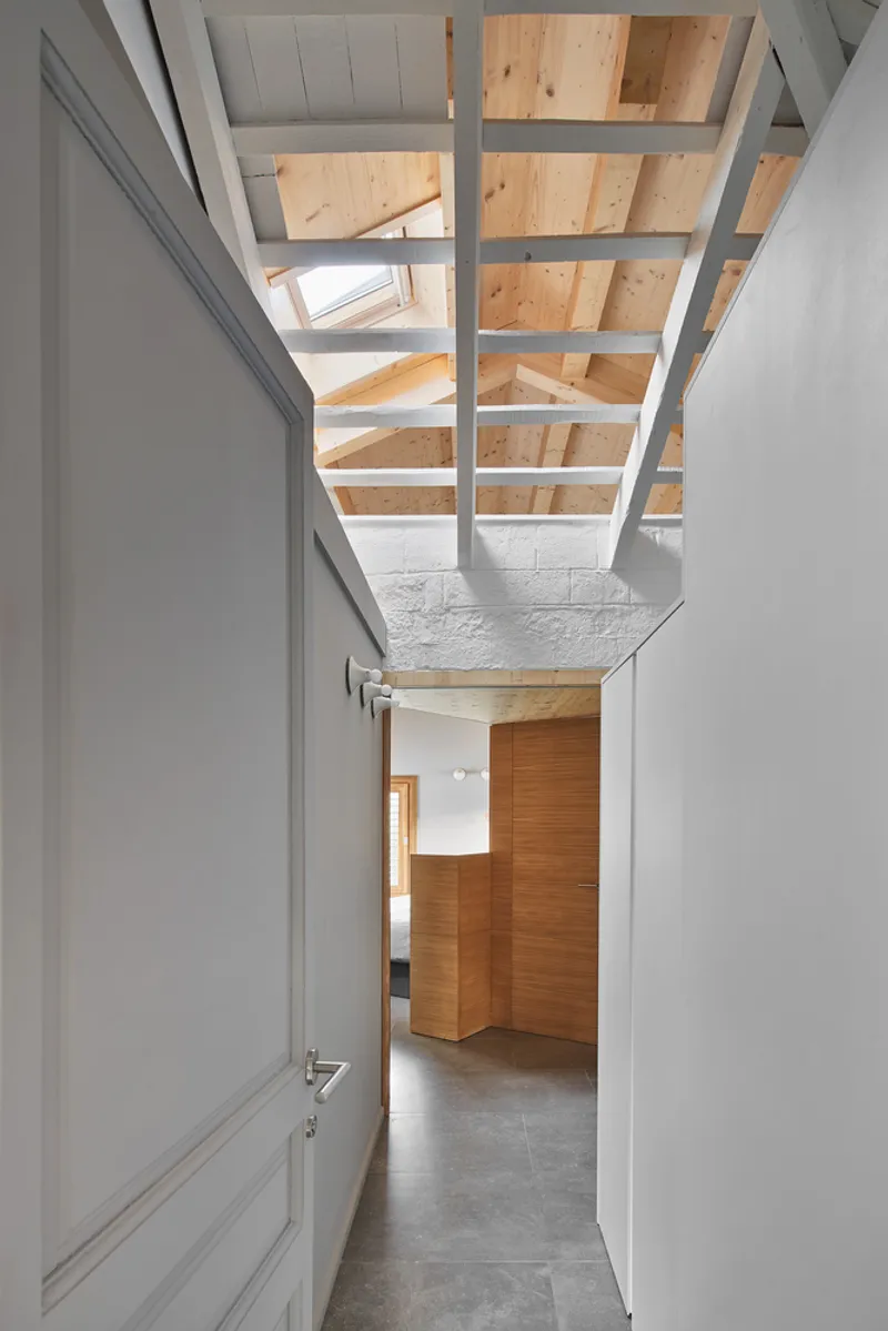 Corridor with exposed timber roof trusses above and timber joinery at the end under natural light