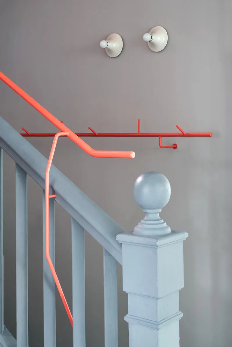 Detail of red tubular handrail intersecting grey balustrade with sphere-topped newel post and wall sconces