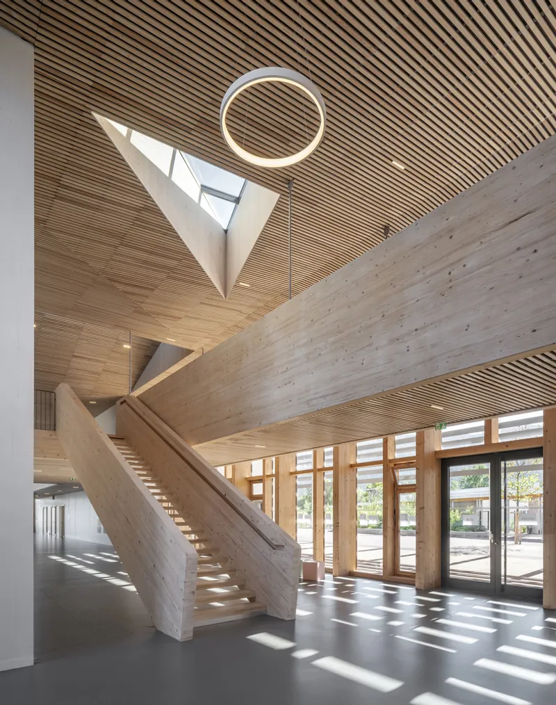 Timber staircase rising beneath triangular skylight and circular pendant light in double-height foyer