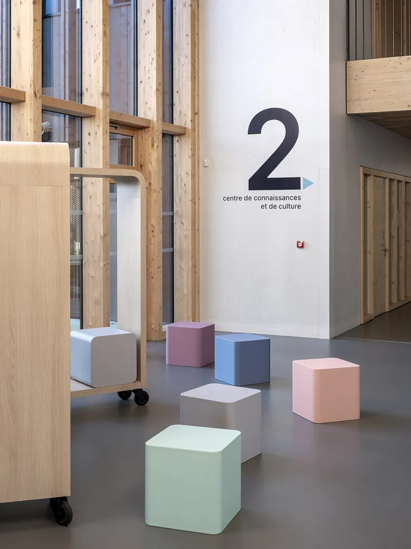 Interior lobby with exposed timber framing and scattered pastel cube seats on polished concrete flooring