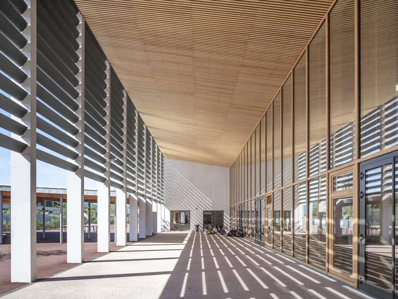 Covered corridor with horizontal timber louvres casting striped shadows across the floor in bright sun
