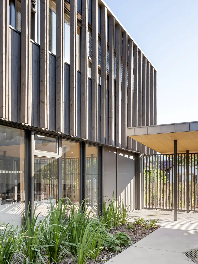 Exterior facade with vertical metal louvers above planted beds and timber pergola structure