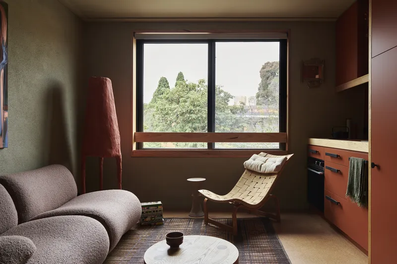 Living room with timber-framed window overlooking green treetops in soft daylight